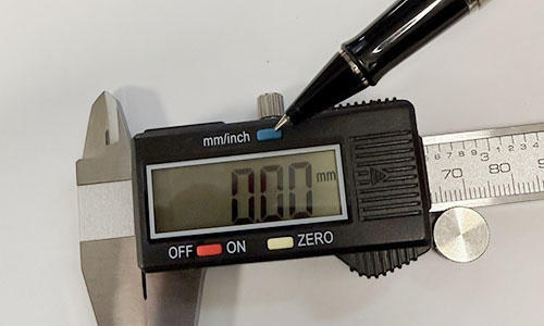 Vinger wijst naar de mm/inch schakelaar op een digitale schuifmaat